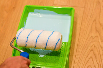 The cylindrical roller absorbs rich blue color from the plastic tray, getting loaded with paint and poised to glide smoothly across the interior surface for a new look.