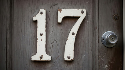 White house number 17 on brown wooden door with metal doorknob white metal numbers keyhole
