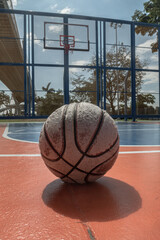 A worn basketball sits on an outdoor court, with a hoop and backboard visible under the Ring Road Bridge in the distance. Space for text.