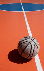 The white court lines contrast sharply with the old basketball's striking appearance and the shadow on the orange court. Copy space.