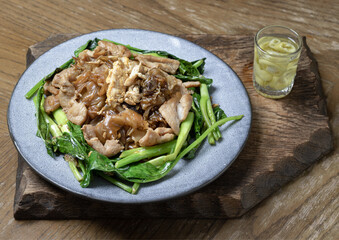 Stir-fried wide rice noodles (Pad See Ew) with soy sauce, pork and Chinese broccoli. The dish is served on a wooden cutting board with pickled chili on the side, a popular Thai street food dish.