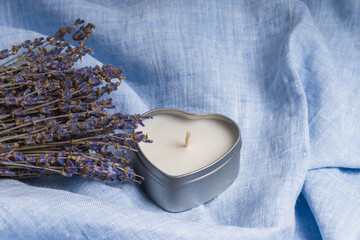 A lavender bouquet next to a heart-shaped candle on a blue linen background.