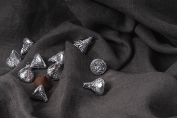 Minimalist gray background of soft linen fabric with beautiful folds and chocolates in silver wrappers.