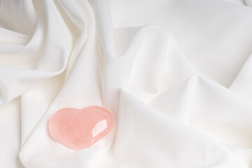 Minimalist composition on soft white fabric with a pink glass heart. Valentine's Day or birthday card.