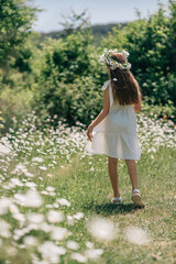 Daisy wreath girl meadow, summer: Child in white dress walks in daisy field during sunny day.