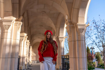 Woman beret architecture. Autumn day: Woman in red poses in stone arches walkway for fashion photoshoot.
