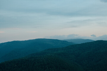 Fototapeta premium A view of blue distant mountains with wisps of fog after sunset, blue landscape