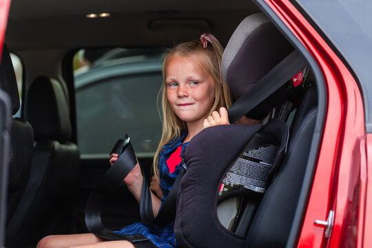 Young school student getting herself buckled into booster seat in car with lap and sash belt
