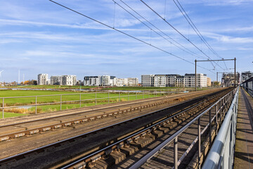 View of railway tracks leading towards the modern residential area Noorderhaven in Zutphen, Netherlands, under a bright blue sky with white clouds.