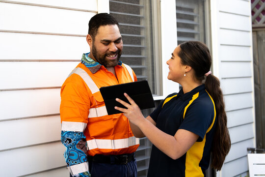 Father and daughter looking at a tablet outside a white weatherboard house