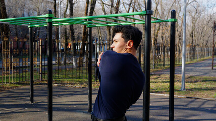 Back view of a muscular man doing pull-ups on a bar in an outdoor park.