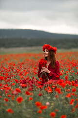 Woman poppy field in red dress and flower crown sits amidst blooming flowers
