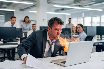 Man spewing fire at laptop in office, concept of failure, anger, frustration, cybersecurity problem or burnout