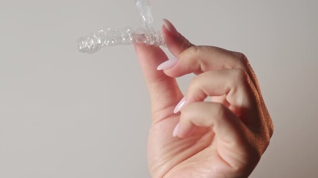 Woman uses dental trays for teeth whitening at home. Girl pours peroxide solution from syringe and applies on teeth, smiling to camera. Neutral background. Female holds trays in a purple case.