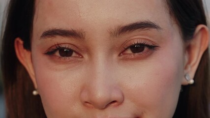 Portrait of young Asian woman with languid brown eyes looks in camera at sunset closeup. Pretty Korean lady face with light daily makeup expresses calmness outdoors. Beauty trends