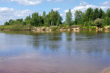 Body of water with a few trees in the background. The water is calm and the sky is blue