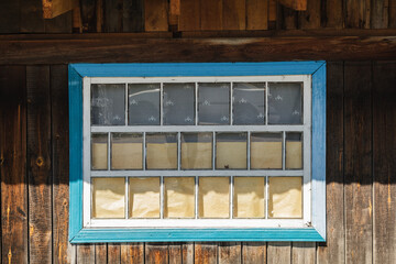 A blue-framed window with white glass in a wooden house in a Siberian village.