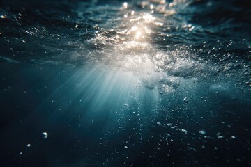 Sunbeams piercing the deep blue ocean surface, illuminating bubbles and turbulent water