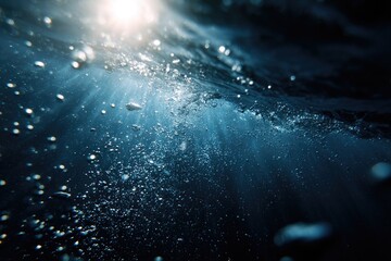Sunbeams pierce deep blue ocean water, illuminating rising air bubbles