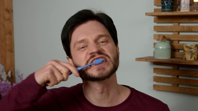 Bearded middle aged man in pajamas doing daily morning routine, brushing teeth with toothbrush for oral hygiene and fresh breath, mouth care for cavity prevention and plaque removal in bathroom