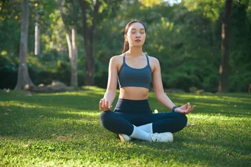 Fotobehang Lotusbloem Young woman meditating in lotus pose outdoors  © Parichat