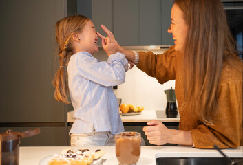Mother and daughter laughing, having fun playful moment in the kitchen at home