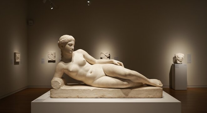 Marble statue of a reclining nude woman on display in a museum surrounded by other artifacts