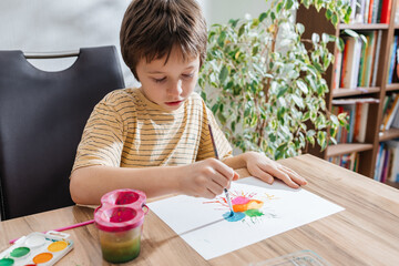 Child painting colorful artwork with brush at table indoors