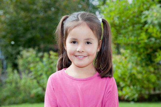 Smiling girl with pigtail hairstyle in pink shirt outdoors in garden