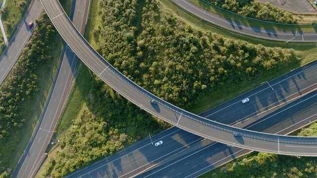 Aerial view of cars driving on a highway interchange in Manukau, Auckland, New Zealand. The roads are surrounded by green trees and grass. The scene shows transportation infrastructure.