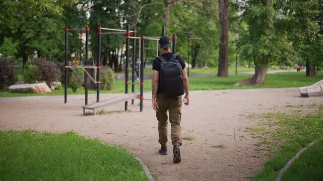 Individual Approaches Open Exercise Zone, Person Advances Into Outdoor Workout Space Confidently, An Athletic Man Carrying Gear Strides Purposefully Into Lush Outdoor Exercise Setting Early In Day