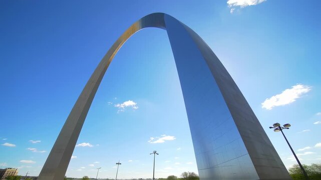 A towering, shiny arch against a vast blue sky with partial buildings and lighting in the scene