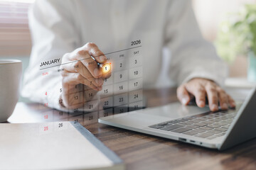 Concept of time management, schedule planning, appointment reminder, genda, deadline, and organizing work plan. Businessman marking with target icon 1 January 2026 calendar virtual screen over laptop.