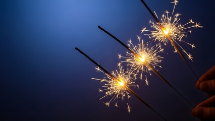 Obraz premium Hands holding burning sparklers against a deep blue sky. Celebration night and festive energy. Bright sparks flying from three sparklers during a New Year or holiday event.