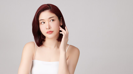 Fototapeta premium A beautiful young Asian woman with clean, fresh skin against a grey background. Skincare, facial treatment, cosmetology, beauty, and spa. An elegant portrait of an Asian woman.