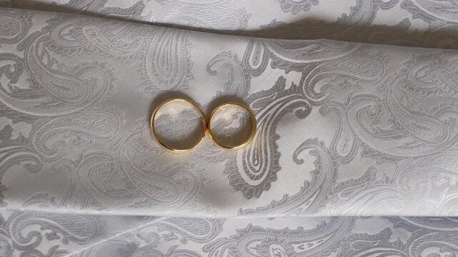 Two gold rings on elegant white paisley fabric, symbolizing love and union