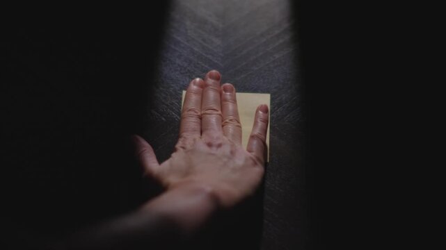 Slow motion close up footage of a hand writing out "February" on a paper note and placing it on a table. Shot in dramatic lighting for an impressive title or transition.