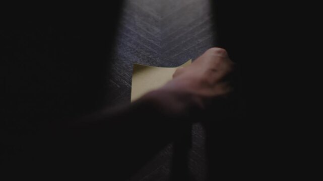 Slow motion close up footage of a hand writing out "September" on a paper note and placing it on a table. Shot in dramatic lighting for an impressive title or transition.