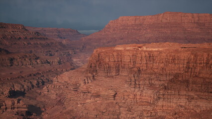 Vast red rock formations rise prominently against a dramatic cloudy sky. The rugged terrain stretches endlessly, revealing natures breathtaking beauty at twilight.