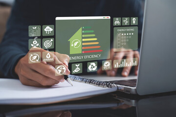 Person working on laptop with virtual interface displaying energy efficiency ratings, sustainability icons, and environmental data, emphasizing green energy solutions and eco-friendly practices.