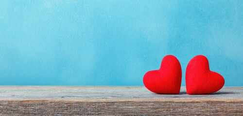 Two plush red hearts sit side-by-side on a rustic wooden surface