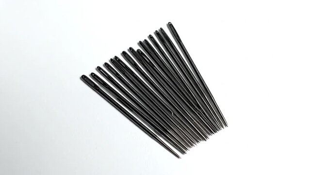 A cluster of dark, metallic sewing needles arranged diagonally against a plain, bright white backdrop