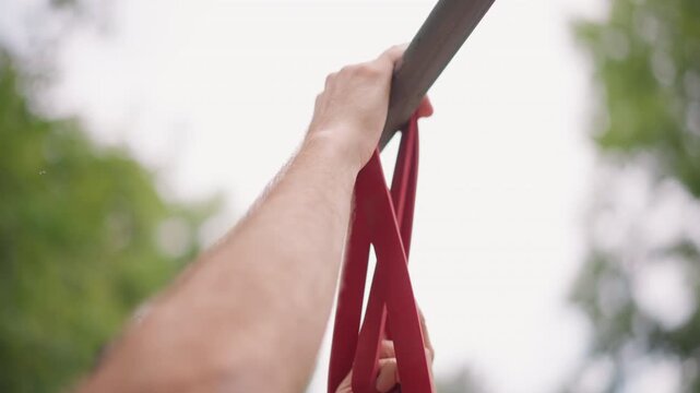 Climber Secures Gear, Holding Strap Around Metal Bar, Person Tightly Grips Red Strap Attached To Metal Bar, Detailed Image Showing Hand Fastening Strap Securely To Metal Rod In Nature Setting