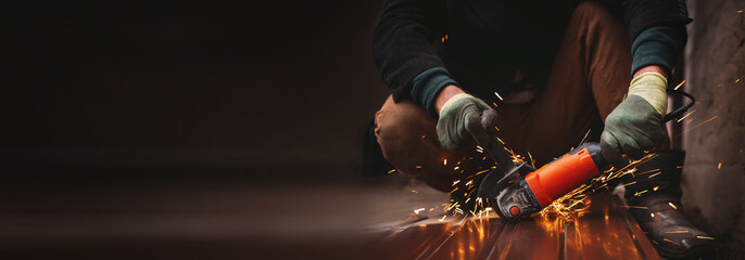A close-up of a worker wearing gloves cutting a sheet of metal with a grinder, sparks flying. An unrecognizable man at a construction site working with metal structures. banner copy space
