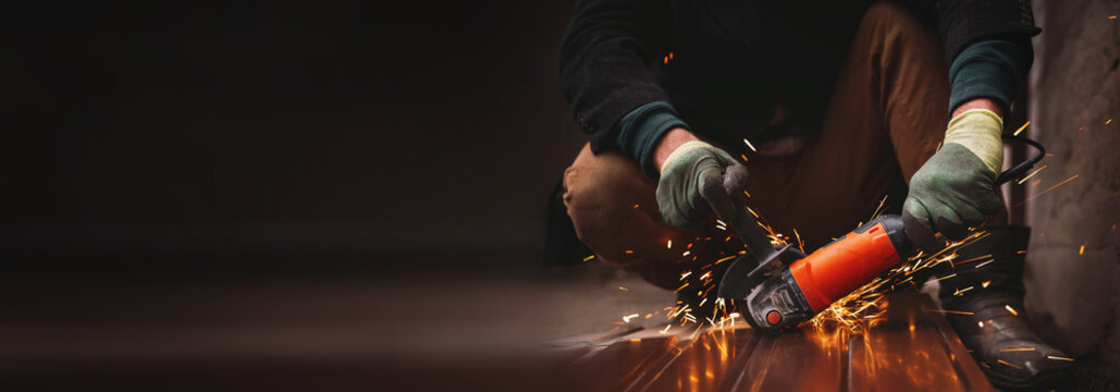 A close-up of a worker wearing gloves cutting a sheet of metal with a grinder, sparks flying. An unrecognizable man at a construction site working with metal structures. banner copy space