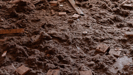 A cluttered room shows a dusty floor covered with pieces of wood and debris. Light from the late afternoon sun highlights the dirt and mess in the area.