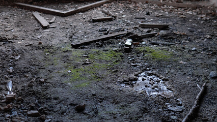 A floor covered with debris and moss shows signs of moisture in an old, abandoned building. Light comes through cracks, highlighting the scattered materials and dirt.