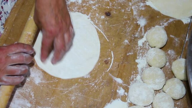 Close-up of an elderly woman's female hands rolling out dough with a wooden rolling pin. Making homemade pies and chebureks.