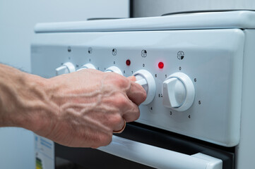 A woman's hand turns on the electric stove using a knob
