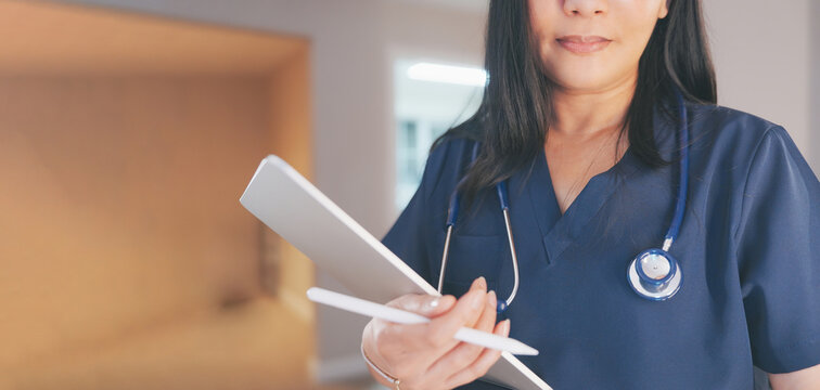 Female doctor in scrubs uses digital tablet,stylus in clinic.Healthcare professional uses modern technology for telehealth,patient data care,medicine management,medical documentation record - Powered by Adobe